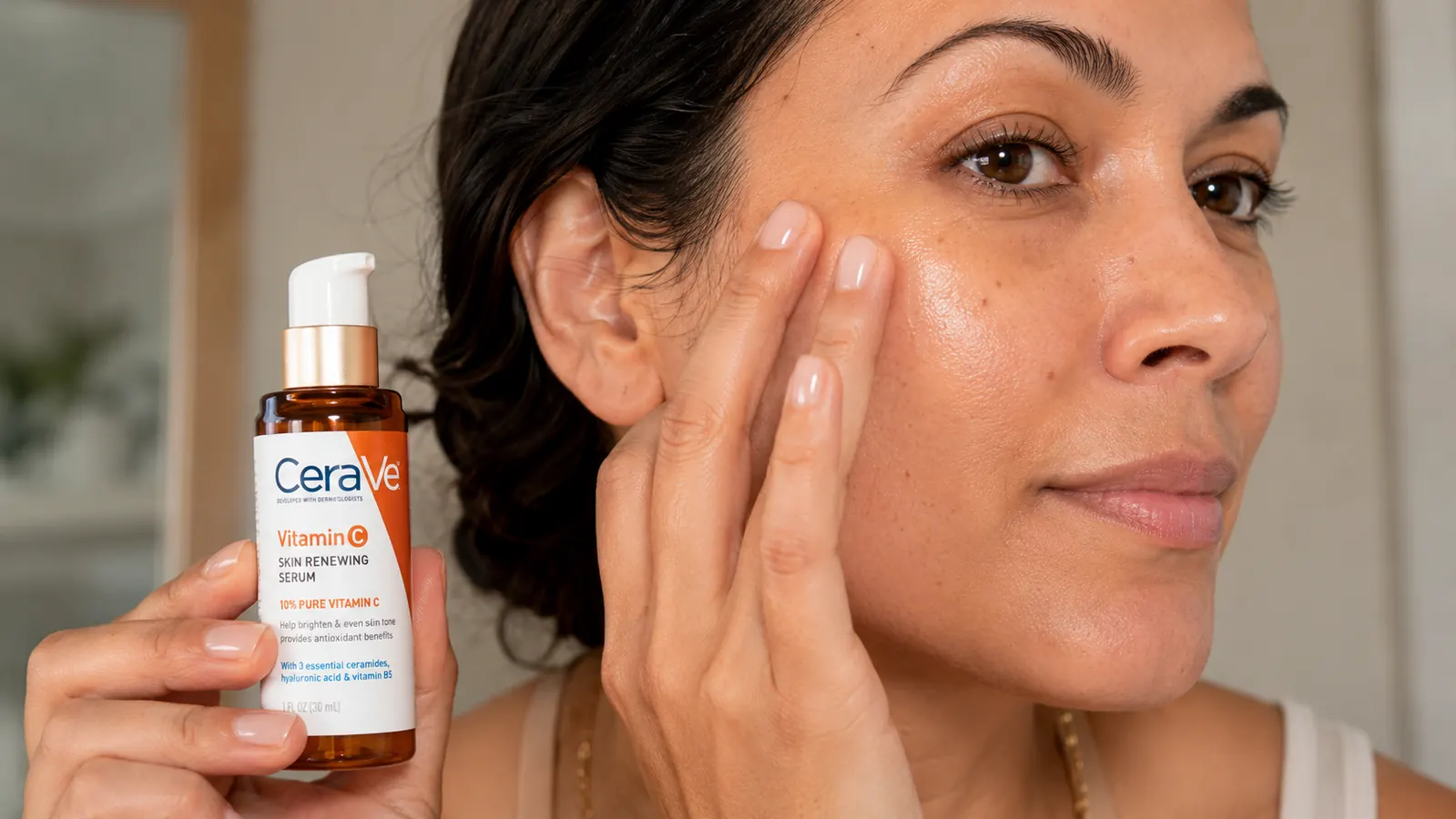 Hand applying a pale-yellow vitamin C serum to clean facial skin, close-up texture shot